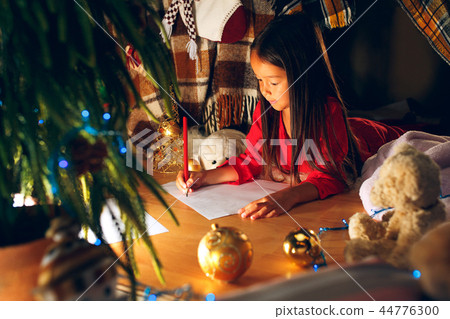 Merry Christmas and Happy Holidays. Cute little child girl writes the letter to Santa Claus near Merry Christmas and Happy Holidays. Cute little child girl writes the letter to Santa Claus near 44776300
