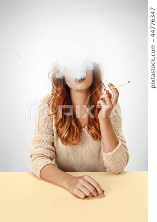 Tranquil woman sitting and smoking resting at the table. Cloud of smoke covering her face. Copy 44776347