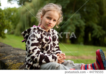 Portrait of a beautiful curly blue-eyed girl sitting on a background of green trees. Vacation in the 44776593