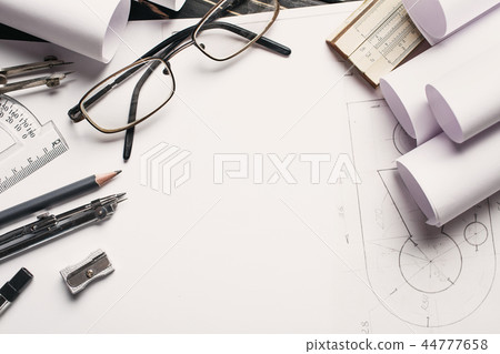 On the wooden table there are drawings, compasses, pencil, elastic, ruler, sharpener and glasses. On the wooden table there are drawings, compasses, pencil, elastic, ruler, sharpener and glasses. 44777658