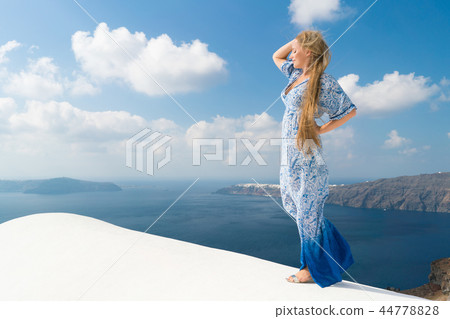 young woman in a white and blue dress enjoys a walk around Santorini 44778828