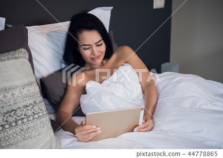 Happy young woman greeting in a tablet video call on line sitting on bed in the bedroom at home 44778865