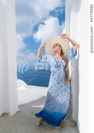 young woman in a white and blue dress enjoys a walk around Santorini 44778898