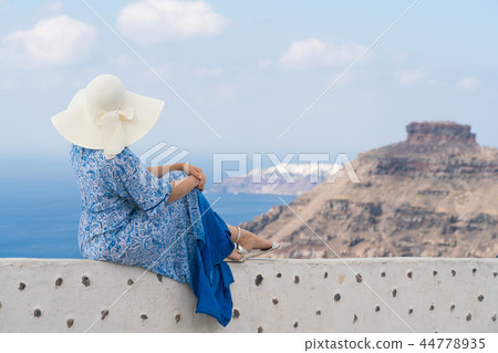young woman in a white and blue dress enjoys a walk around Santorini 44778935