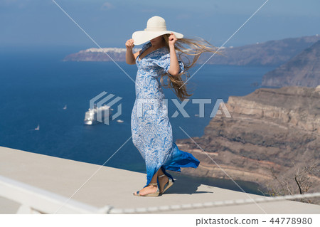 young woman in a white and blue dress enjoys a walk around Santorini 44778980