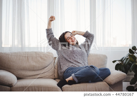 Young woman relaxing on a couch in living room Young woman relaxing on a couch in living room 44780167
