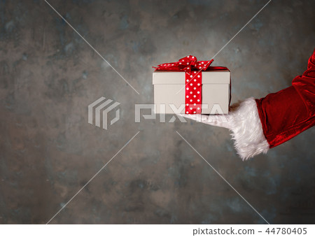 Santas hand holding a giftbox with red bow Santas hand holding a giftbox with red bow 44780405