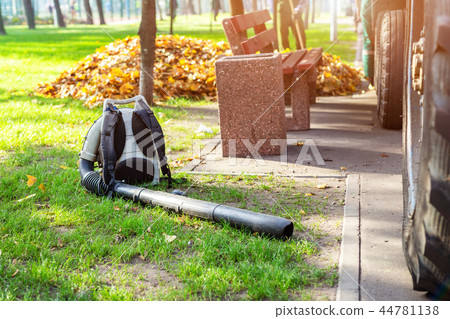 Heavy duty foliage blower lying on clean grass in city park in autumn. Seasonal leaves cleaning and Heavy duty foliage blower lying on clean grass in city park in autumn. Seasonal leaves cleaning and 44781138