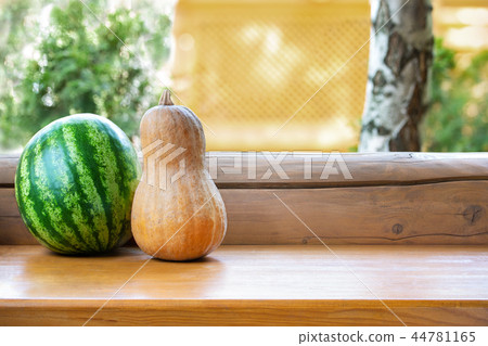Ripe orange pumpkin and green striped watermelon on wooden table outdoors. Agriculural harvest Ripe orange pumpkin and green striped watermelon on wooden table outdoors. Agriculural harvest 44781165
