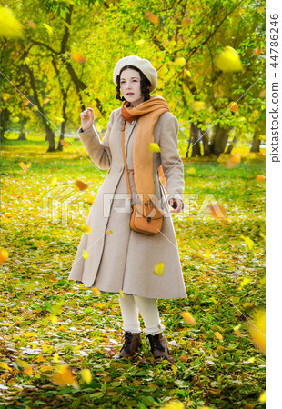 Girl in autumn on walk looks at the falling leaves 44786246