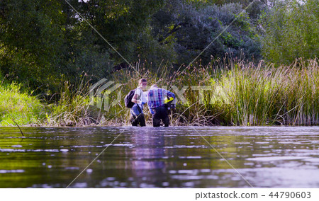 Two scientists ecologists in high rubber boots walking in the water of the forest river Two scientists ecologists in high rubber boots walking in the water of the forest river 44790603
