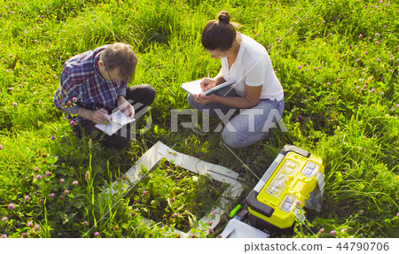 Two ecologist examining plants on the meadow 44790706