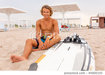 Handsome man sits on the beach with white blank surfing board wait for wave to surf spot at sea 44800193