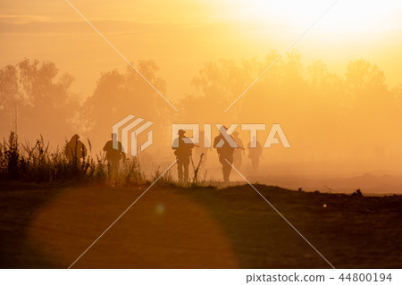 silhouette action soldiers walking hold weapons the background is smoke and sunset. War, military silhouette action soldiers walking hold weapons the background is smoke and sunset. War, military 44800194