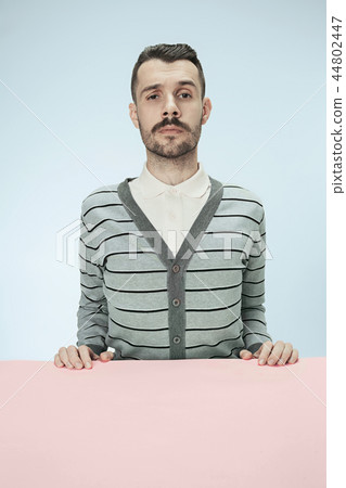 Serious business man sitting at a table on a blue background Serious business man sitting at a table on a blue background 44802447