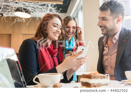 Three young friends using a mobile phone for fun during a coffee break Three young friends using a mobile phone for fun during a coffee break 44802502