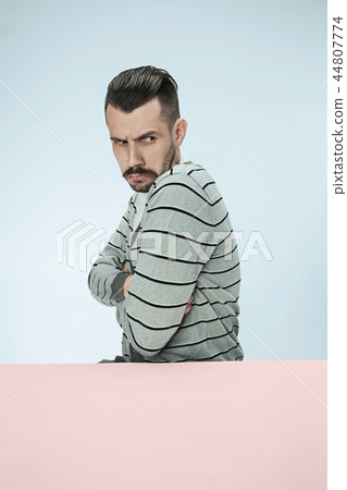 Serious suspicious business man sitting at a table on a blue background Serious suspicious business man sitting at a table on a blue background 44807774