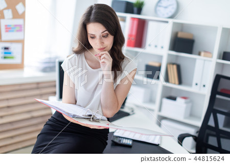 A young girl sat down on a table in the office and holding a red folder. 44815624