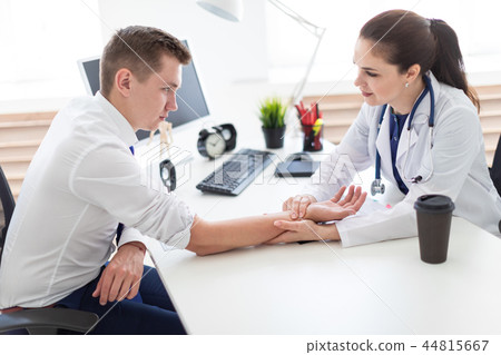 The young man came to see the doctor. The doctor measures the pulse of the patient. 44815667