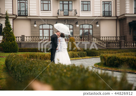 Groom and bride walking in the park on their wedding day. Autumn weather. Rair. Couple umbrella 44826912
