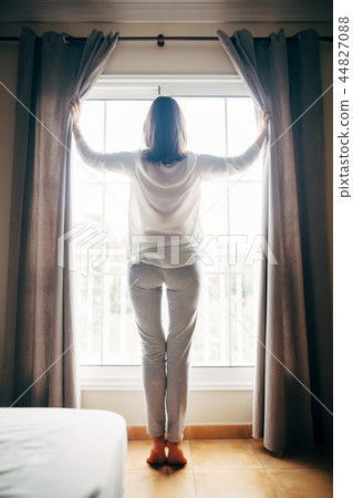 Beautiful young woman wake up and open the curtains on window Beautiful young woman wake up and open the curtains on window 44827088
