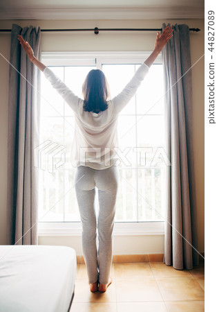 Full length portrait of happy woman stretching near window after Full length portrait of happy woman stretching near window after 44827089