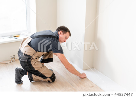 Male worker installing new wooden laminate flooring on a warm film foil floor. infrared floor Male worker installing new wooden laminate flooring on a warm film foil floor. infrared floor 44827447
