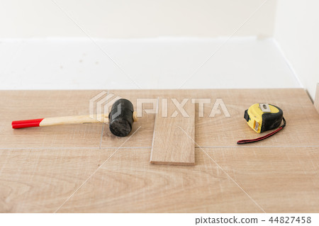 Installing laminate parquet in interior. On the floor lie different carpenter tools. Hammer and 44827458
