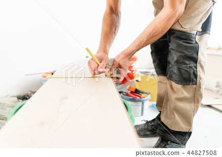 Male worker applies markings to the Board for cutting with a electrofret saw. installing new wooden Male worker applies markings to the Board for cutting with a electrofret saw. installing new wooden 44827508