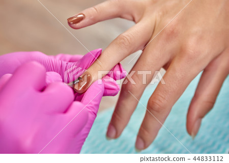 Closeup of process of covering nails with brown varnish in beauty salon. Closeup of process of covering nails with brown varnish in beauty salon. 44833112