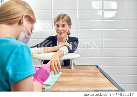 Woman in office suit talking with beautician while she doing manicure in salon. Woman in office suit talking with beautician while she doing manicure in salon. 44833117