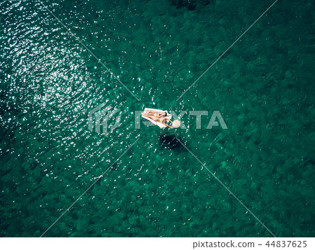 Two young beautiful Caucasian women lying on a mattress in calm azure water Two young beautiful Caucasian women lying on a mattress in calm azure water 44837625