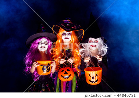 Three Beautiful girl in a witch costume on a dark background in smoke scaring and making faces Three Beautiful girl in a witch costume on a dark background in smoke scaring and making faces 44840751