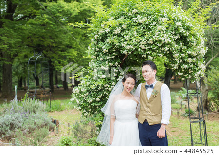 Bride and groom smiling under an arch of roses Bride and groom smiling under an arch of roses 44845525