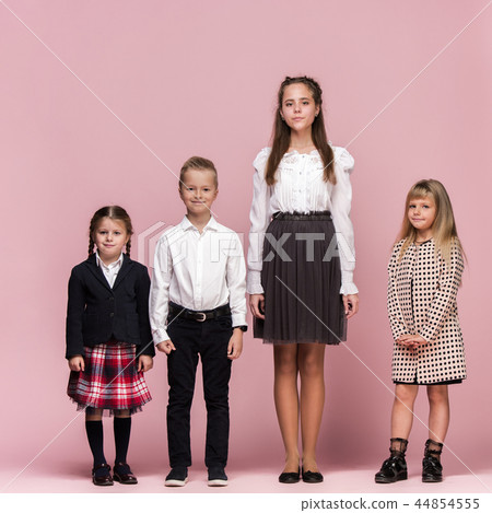 Cute stylish children on pink studio background. The beautiful teen girls and boy standing together 44854555