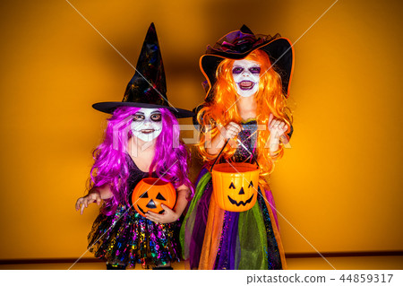 Two Beautiful girl in a witch costume on a yellow background scaring and making faces 44859317
