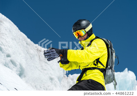Professional skier in a helmet with a backpack and a ski mask standing on a glacier is preparing to 44861222