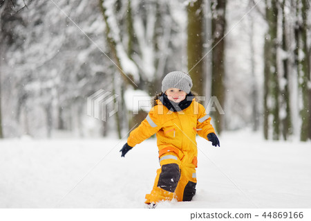 Cute little boy in yellow winter clothes walks during a snowfall 44869166
