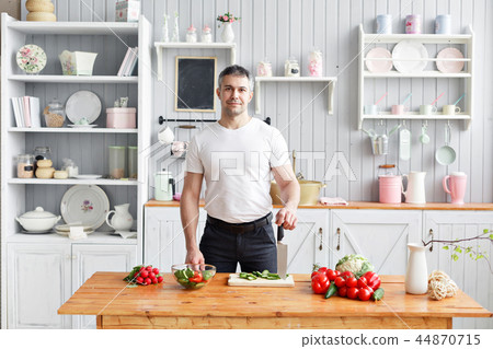 Portrait of handsome smiling man chopping vegetables in the kitchen. The concept of eco-friendly Portrait of handsome smiling man chopping vegetables in the kitchen. The concept of eco-friendly 44870715