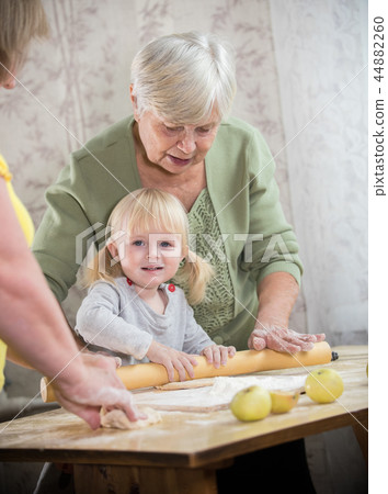 An old lady making little pies with a little girl. Girl looking in the camera An old lady making little pies with a little girl. Girl looking in the camera 44882260