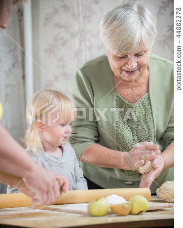 An old lady making little rounded pies with a little girl An old lady making little rounded pies with a little girl 44882278