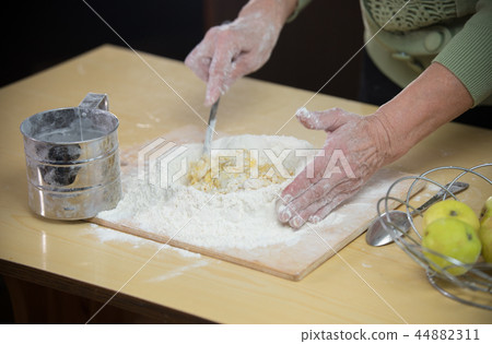 An old lady making little pies with apple pieces 44882311