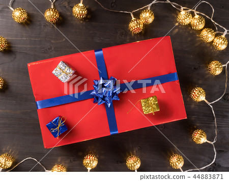 Red christmas gift box with smaller gift boxes on dark wooden floor surrounded by golden lights Red christmas gift box with smaller gift boxes on dark wooden floor surrounded by golden lights 44883871