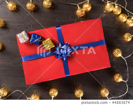 Red christmas gift box with smaller gift boxes on dark wooden floor surrounded by golden lights Red christmas gift box with smaller gift boxes on dark wooden floor surrounded by golden lights 44883874