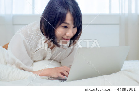 Woman operating a computer in bed Woman operating a computer in bed 44892991