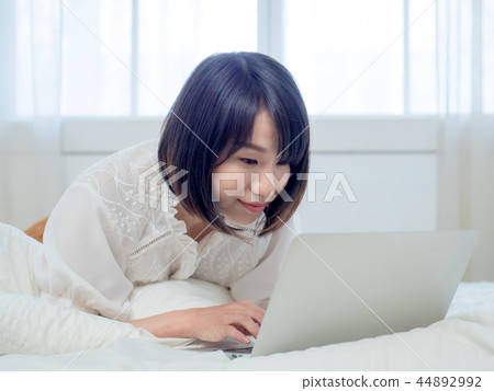 Woman operating a computer in bed Woman operating a computer in bed 44892992