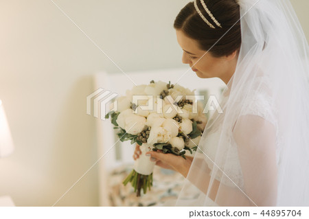 Beautiful and tenderness bride in white dress and veil. Hold bouquet of flowers in hands 44895704