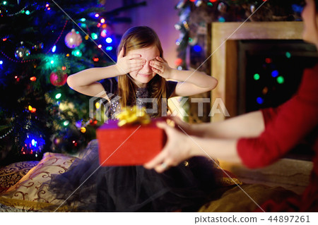 Happy little girl getting a Christmas gift from her mommy Happy little girl getting a Christmas gift from her mommy 44897261