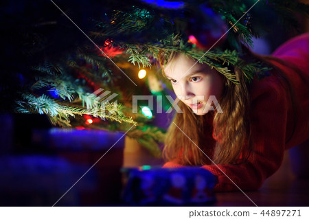 Adorable little girl looking for gifts under a Christmas tree 44897271