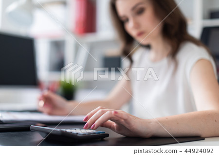 A young girl sitting in the office at a computer Desk and counting on a calculator. Photo with depth 44924092